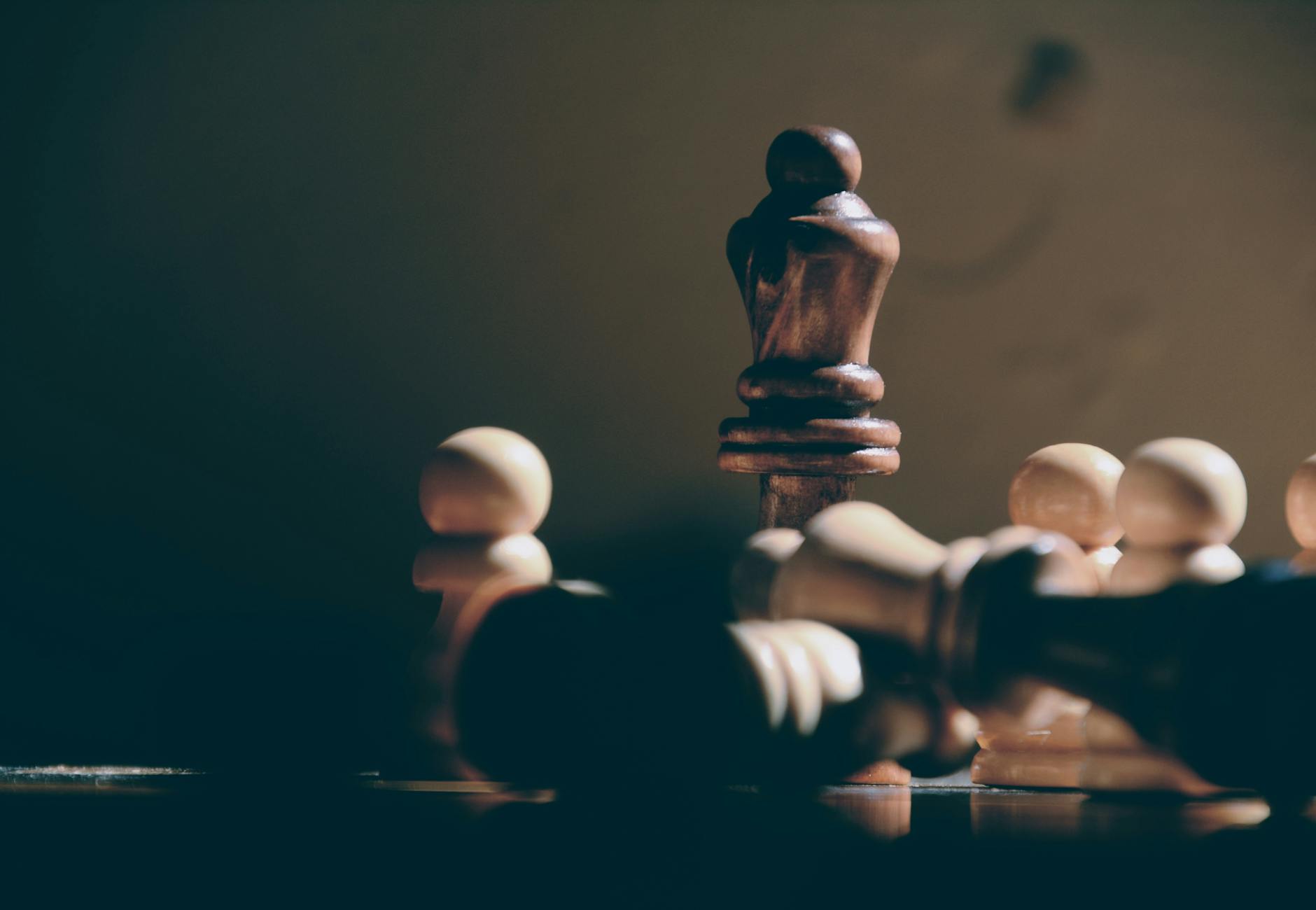 Close-up of a standing chess piece surrounded by fallen pieces, in moody lighting.