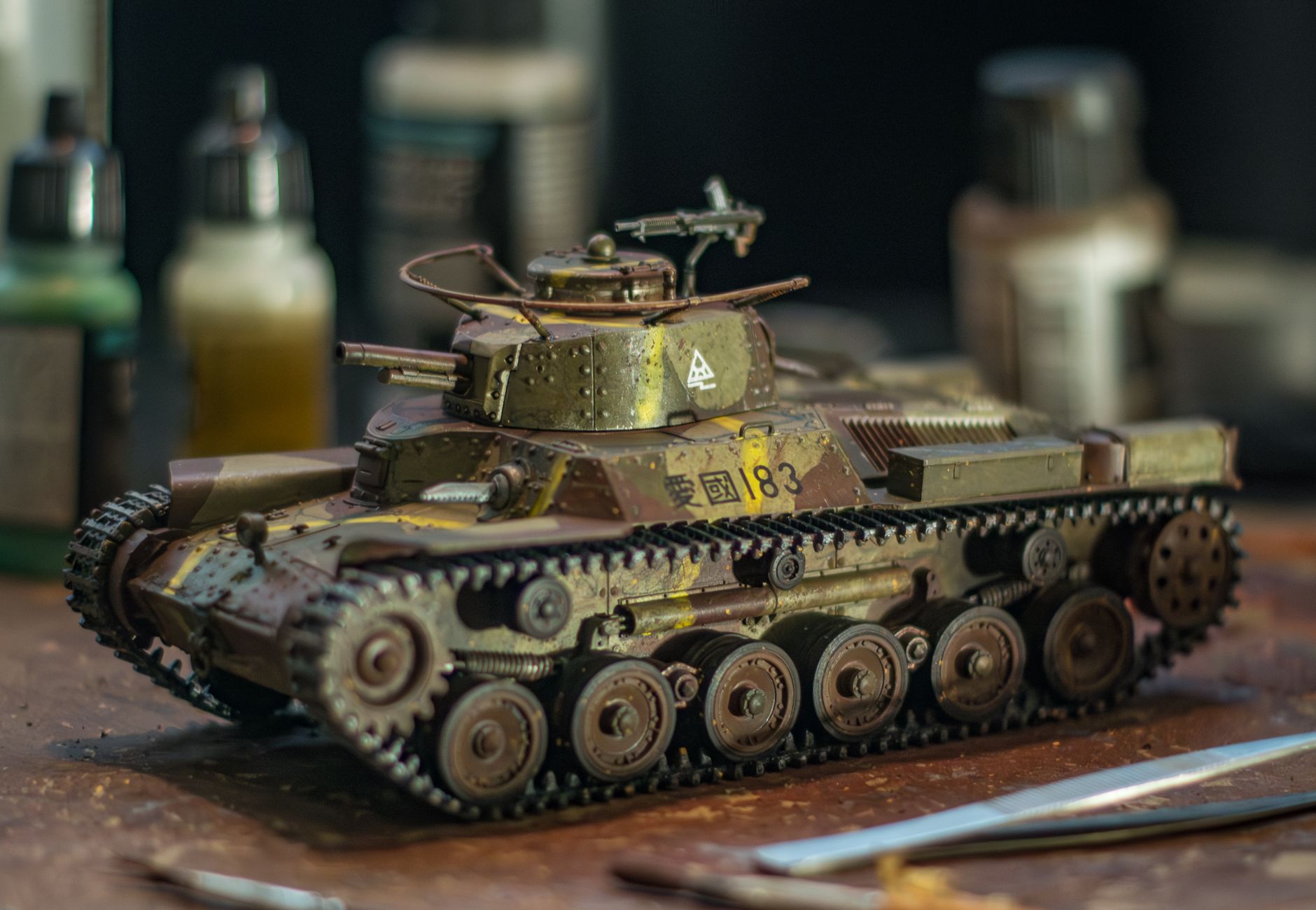 Close-up of a detailed model tank on a crafting workspace with paint bottles in the background.