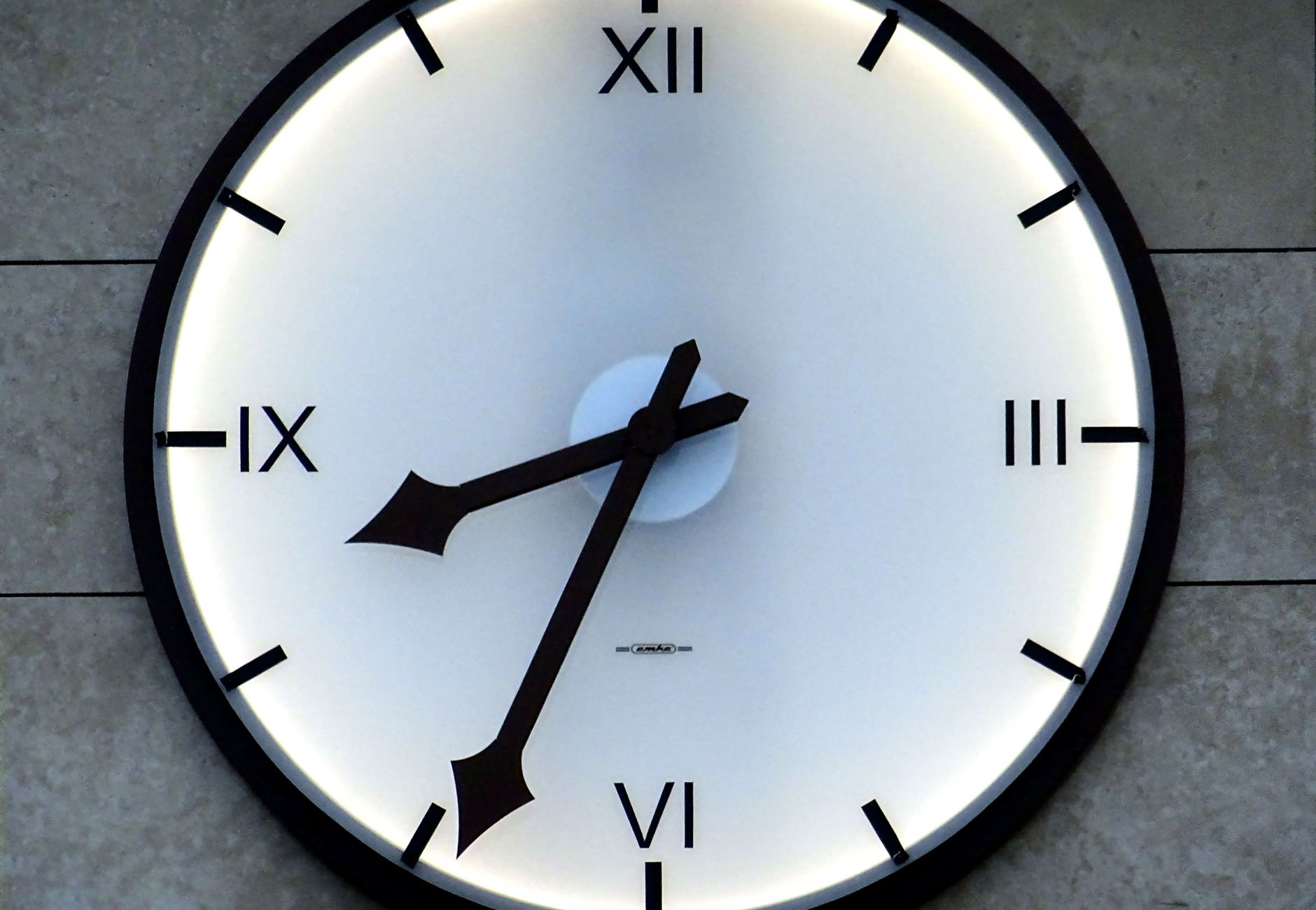 Close-up of a modern wall clock with Roman numerals and backlit design, emphasizing timekeeping precision.